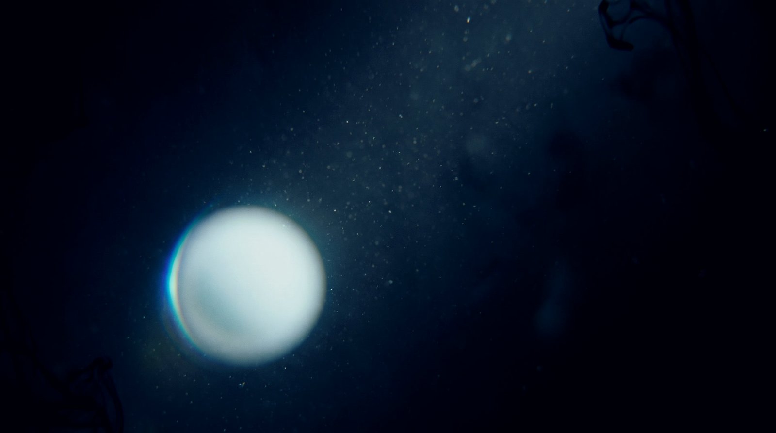 A luminous white orb close up in dark water, a thin prismatic edge along one side